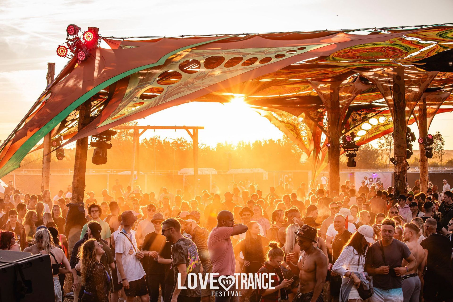 Menschenmenge tanzt bei Sonnenuntergang unter einem Blätterdach auf einem Open-Air-Musikfestival.