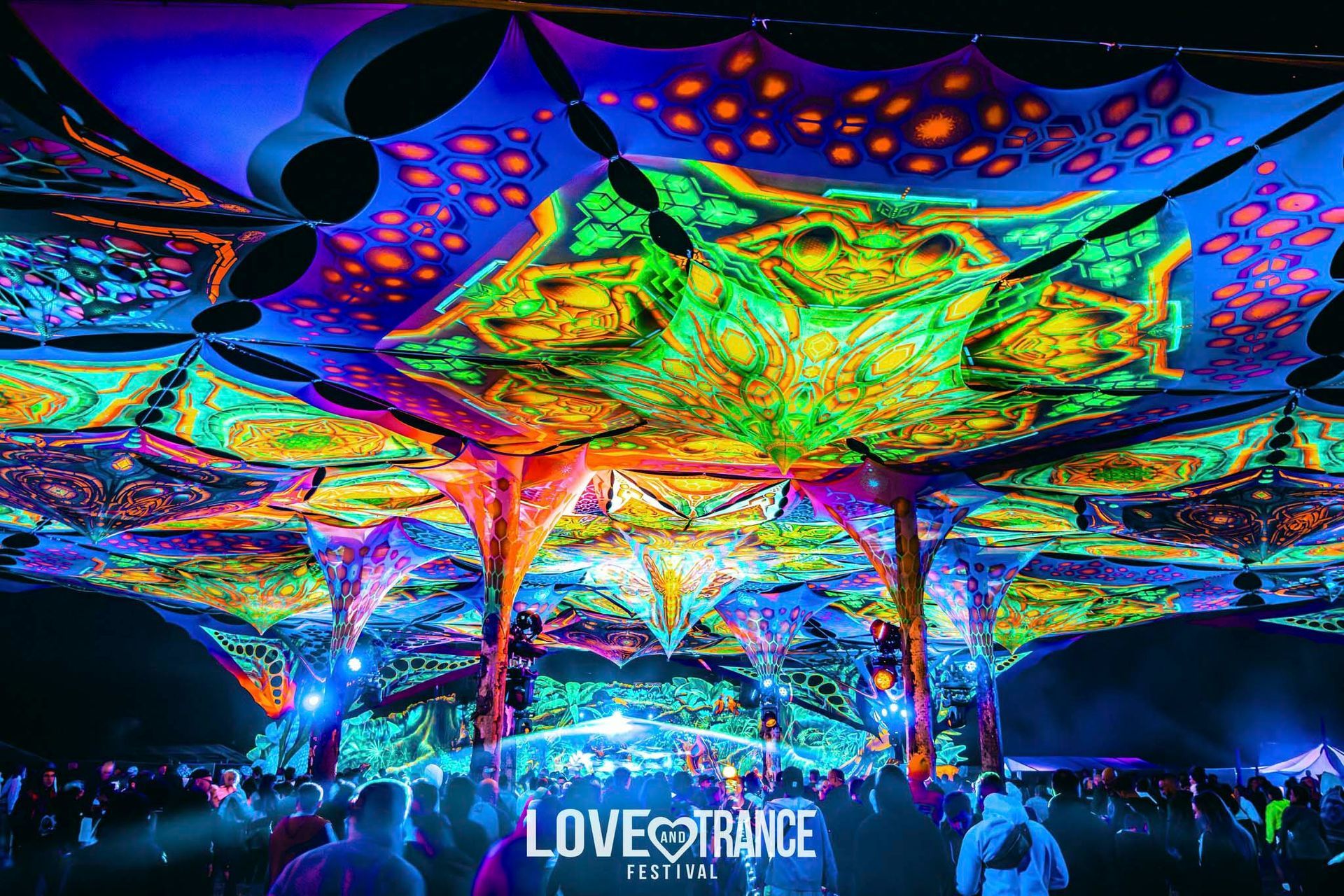 Psychedelisches Zelt auf einem Festival; leuchtende Lichter und Muster in kräftigen Farben. Logo des „Love Trance Festivals“.