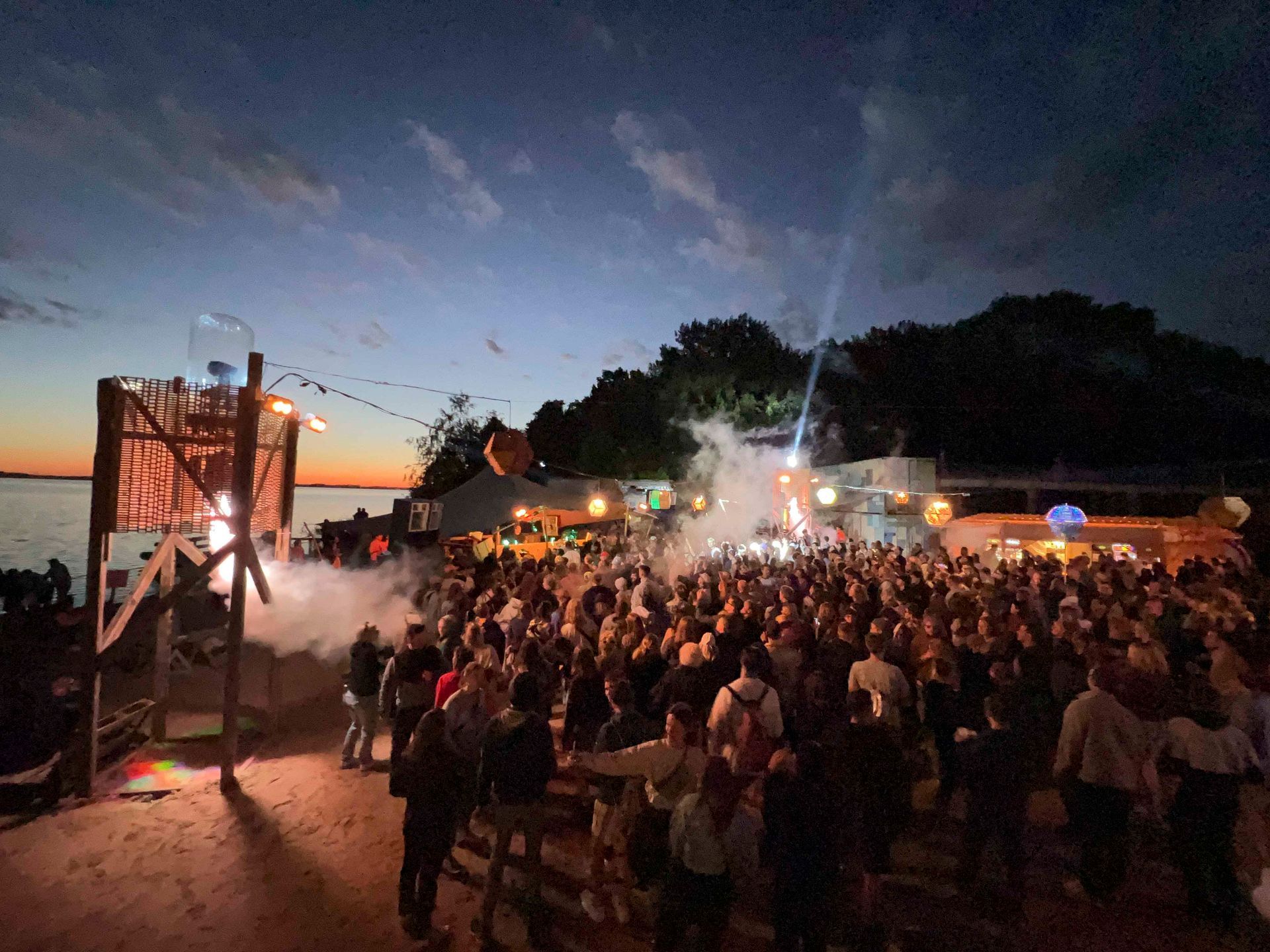 Großes Open-Air-Konzert mit einer tanzenden Menschenmenge in der Nähe der Bühne in der Abenddämmerung.