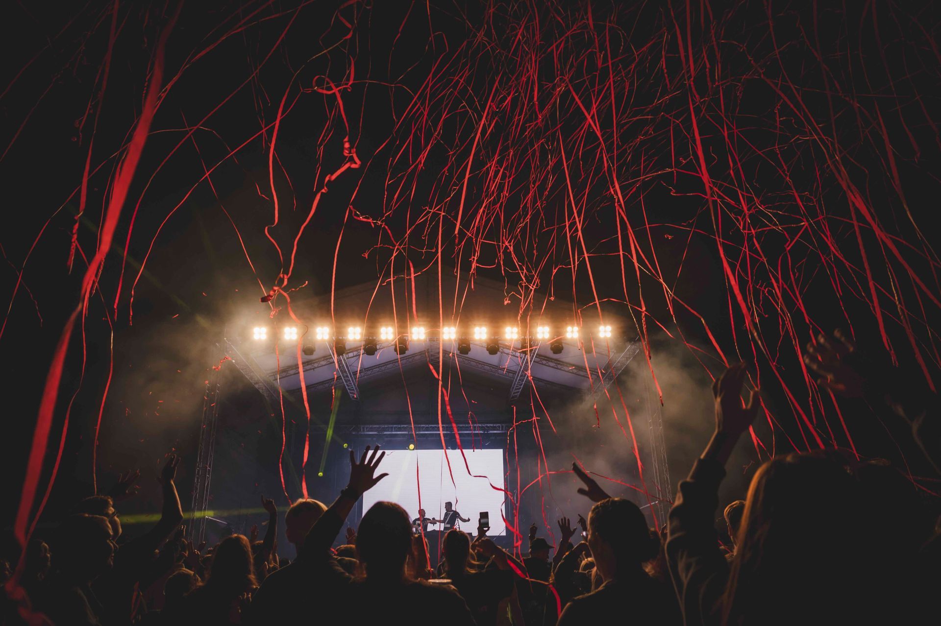 Konzertbühne mit rotem Konfetti, hellem Licht und Publikum mit erhobenen Armen.