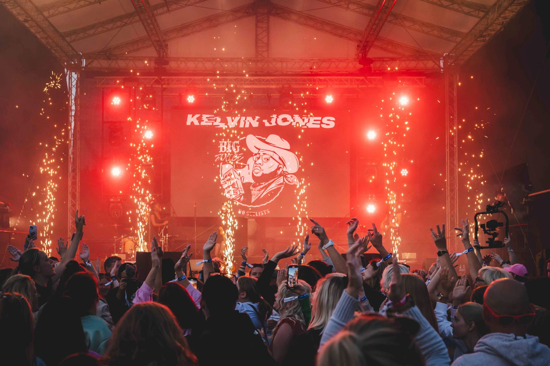Kelvin Jones Konzert: Die Menge jubelt vor der Bühne mit Logo, Pyrotechnik und roten Lichtern.