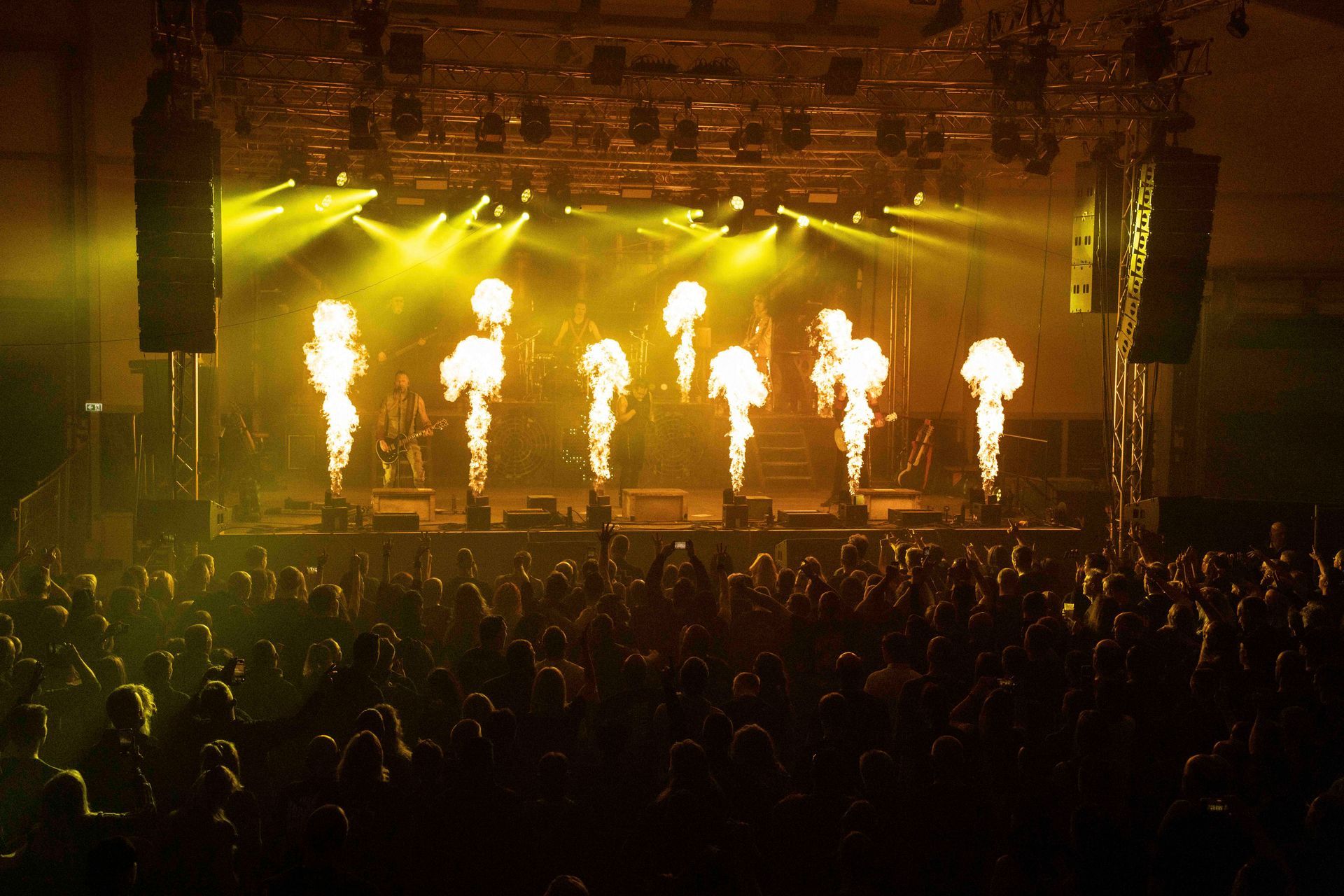 Konzertbühne mit Pyrotechnik, hellgelben Lichtern und einer Menschenmenge.