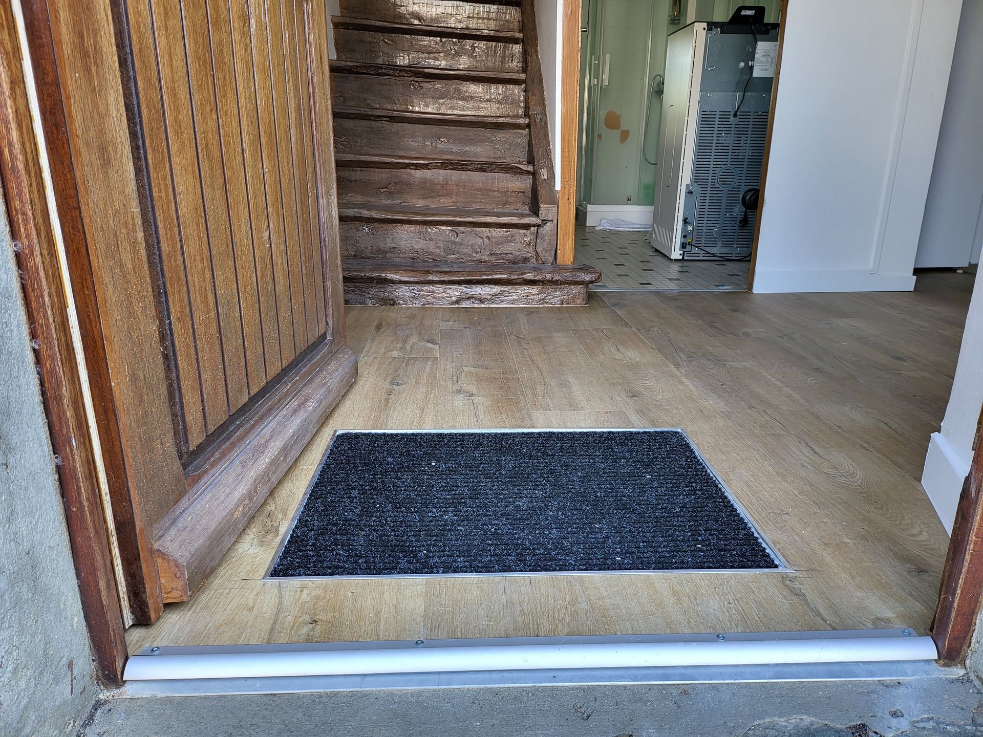 Porte d'entrée ouverte sur un sol en PVC imitation bois.