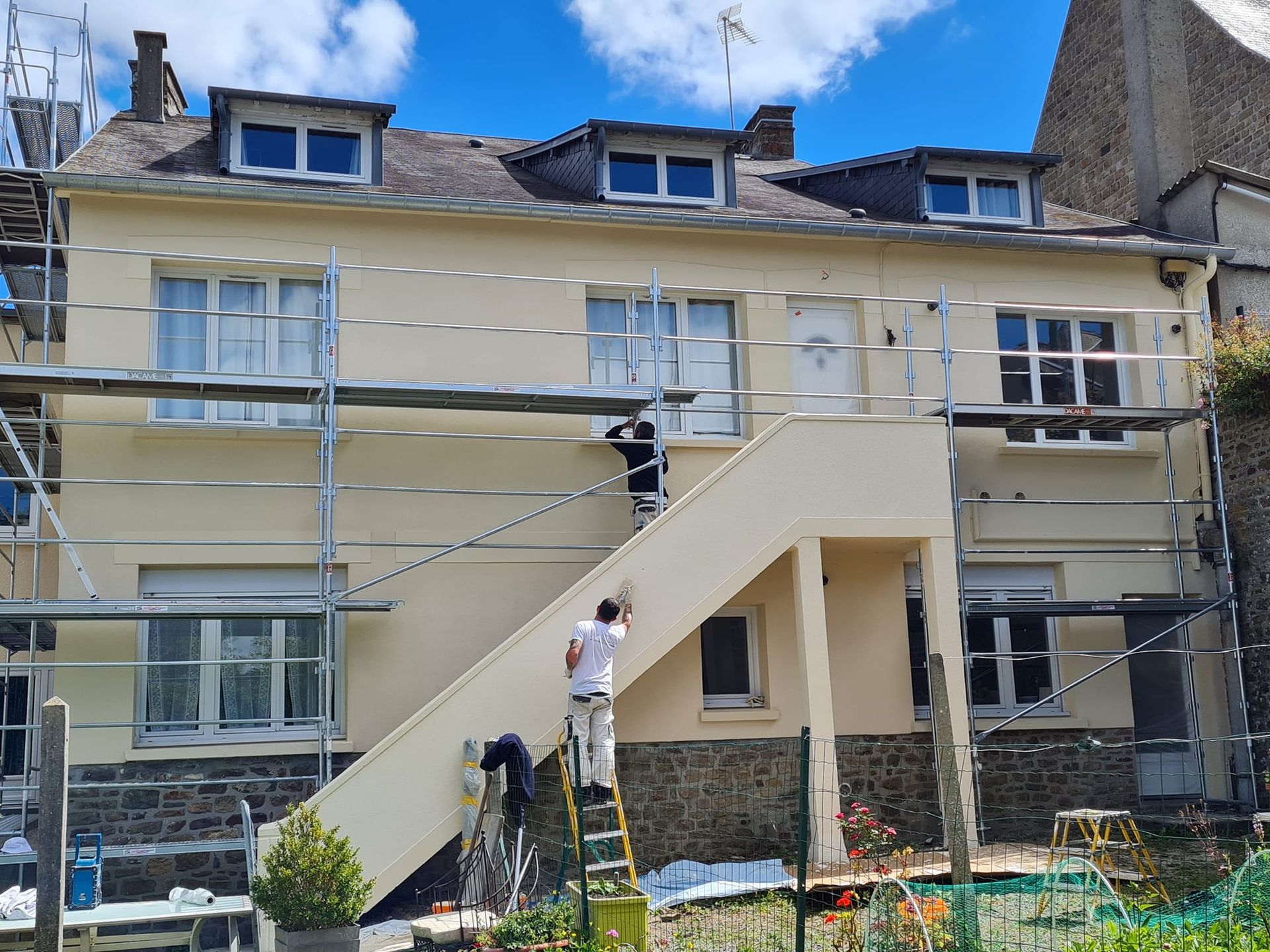 Un échafaudage sur la façade d'une maison avec des peintres.