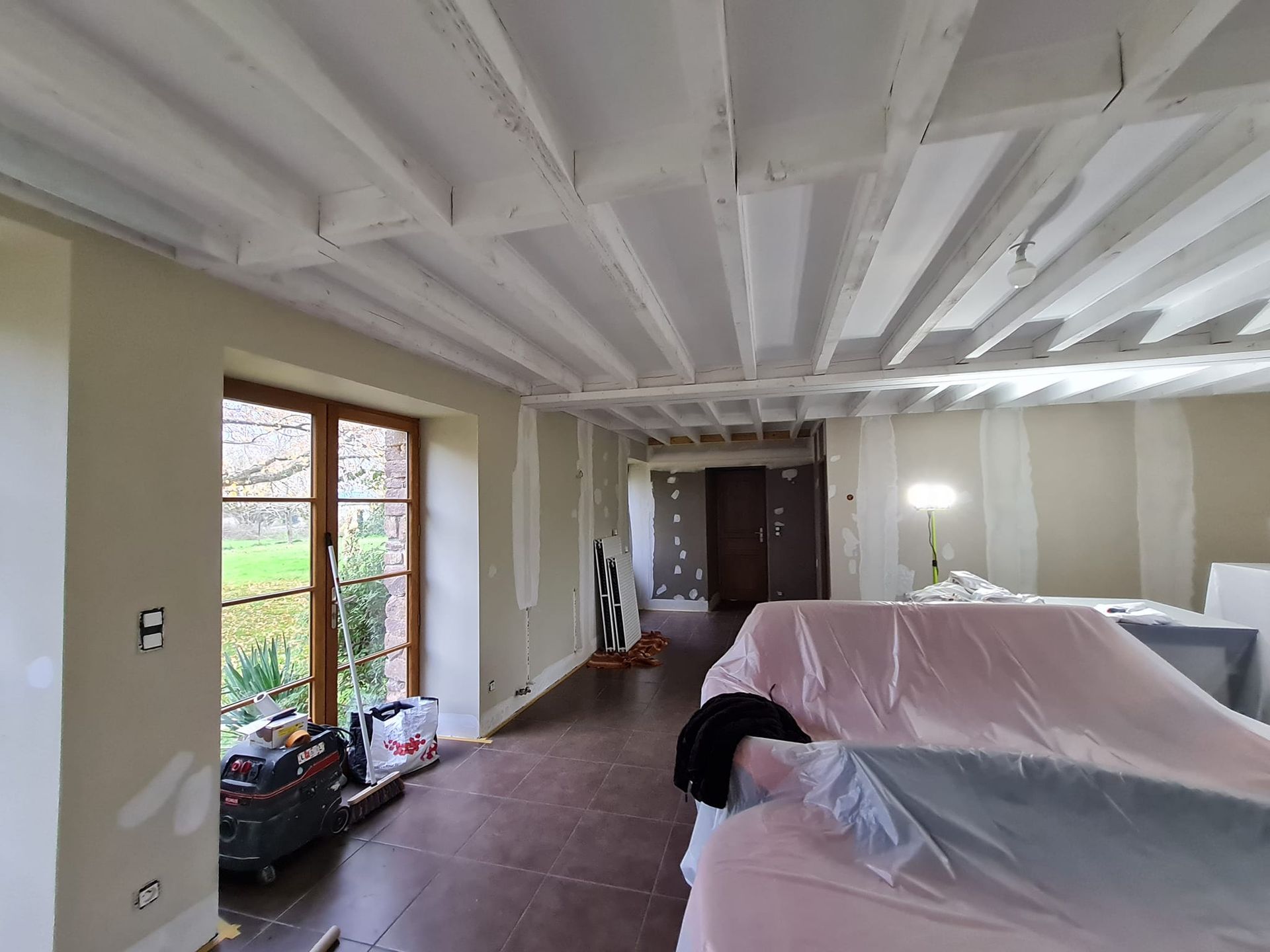 Travaux de peinture dans un grand salon aux poutres apparentes.