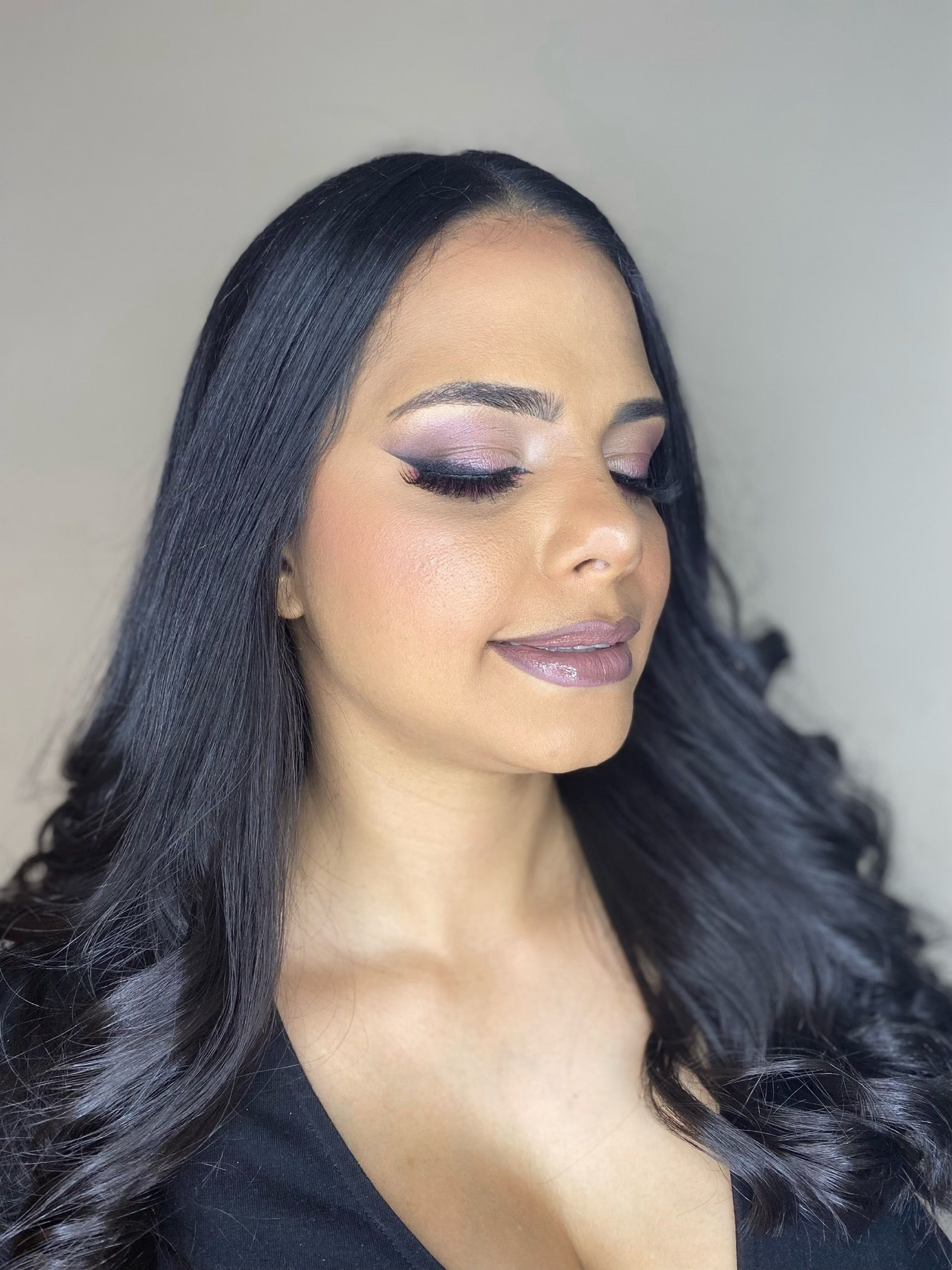 Una mujer con cabello largo y negro y sombra de ojos rosa lleva una blusa negra.