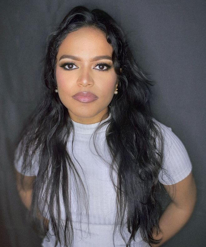 Una mujer con cabello largo y negro lleva una camisa blanca y aretes.