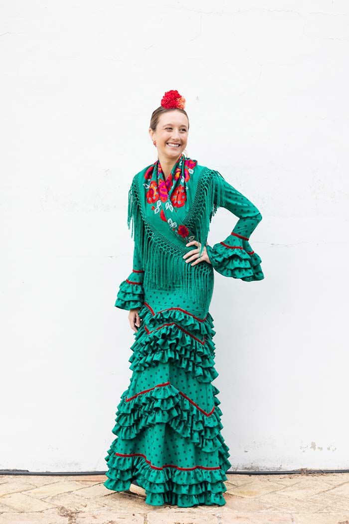Mujer con un vestido flamenco verde con volantes posando contra una pared blanca.