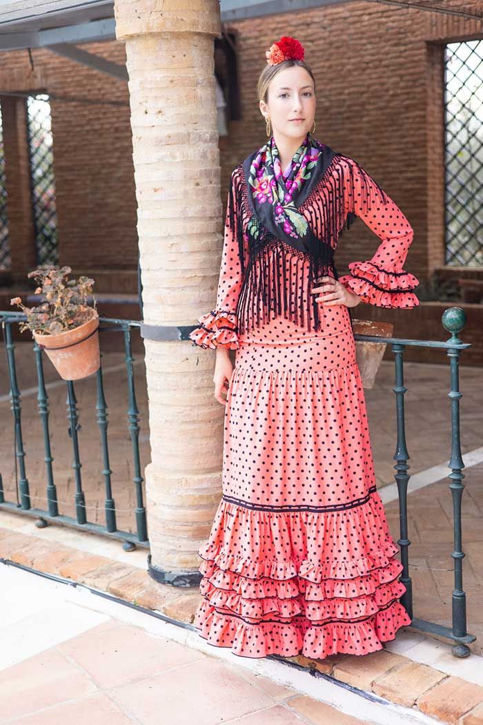 Mujer con vestido de flamenco rojo de pie junto a una barandilla en un patio de ladrillos.