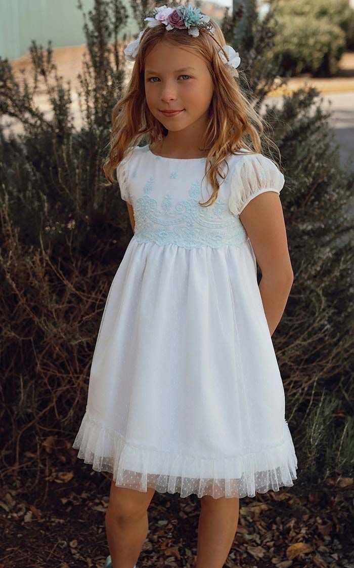 Niña con un vestido blanco de pie al aire libre entre arbustos.