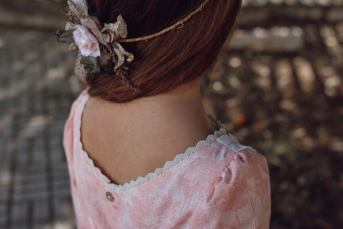 Primer plano de la espalda de una persona con un vestido rosa de encaje y un accesorio floral en el cabello.