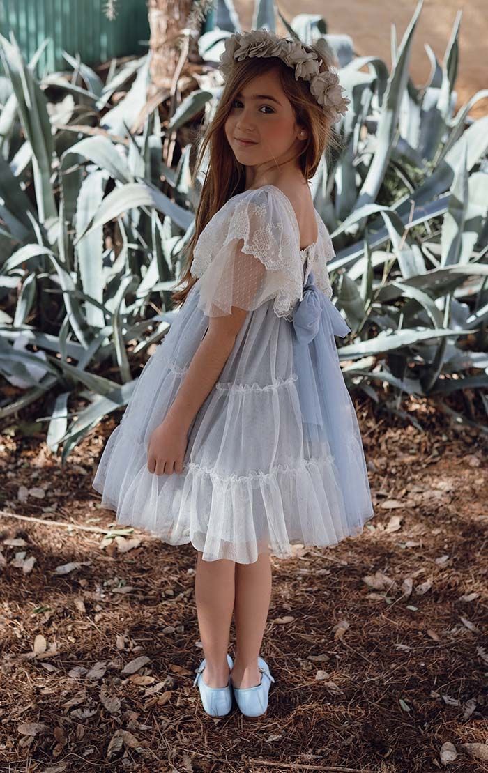 Niña con vestido blanco y corona de flores de pie al aire libre entre grandes plantas de agave.