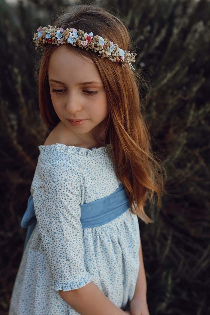 Niña con vestido blanco y diadema floral mirando hacia abajo al aire libre