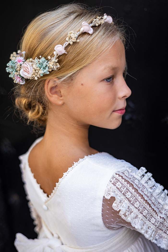 Perfil de una chica con un vestido blanco de encaje y una diadema floral, mirando hacia la derecha sobre un fondo oscuro.