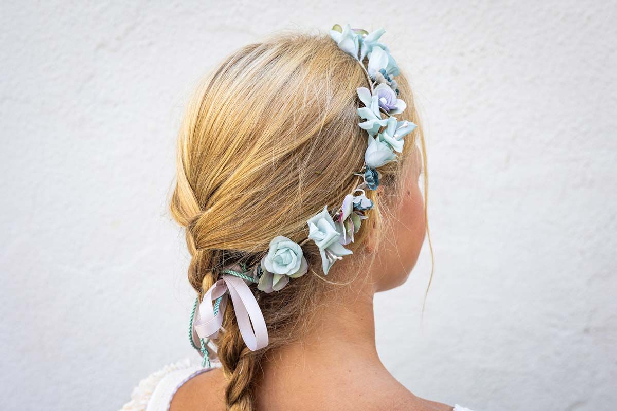 Cabello rubio trenzado adornado con flores azul pálido contra una pared blanca.