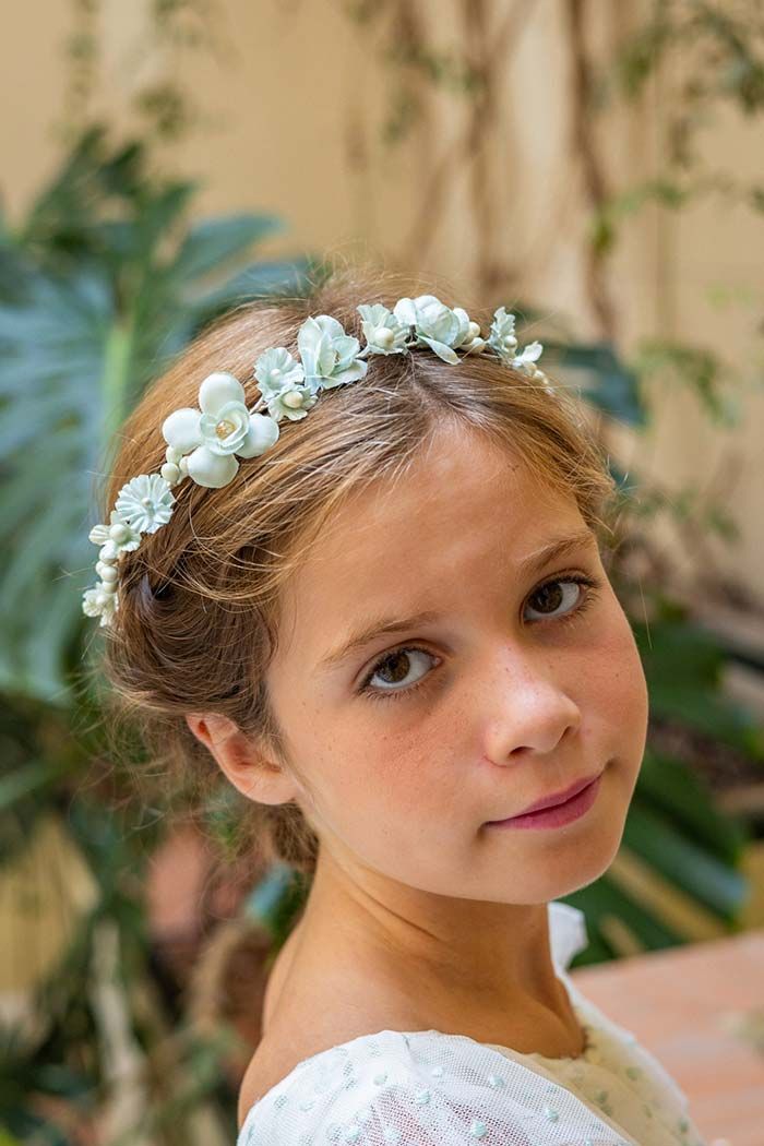 Retrato de una niña con una diadema blanca de flores, mirando a la cámara al aire libre.