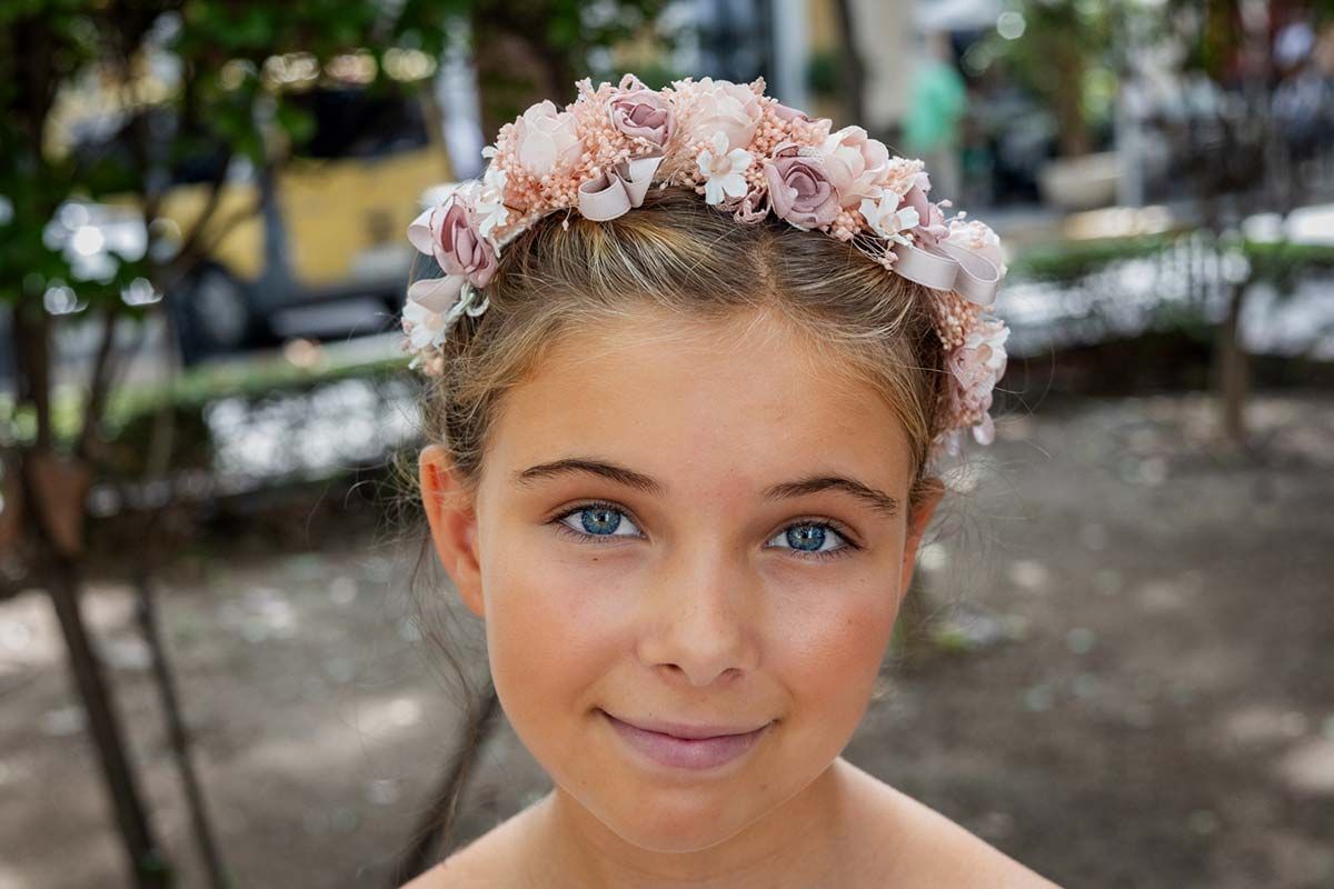 Retrato de cerca de una niña sonriente con una corona de flores rosas al aire libre.