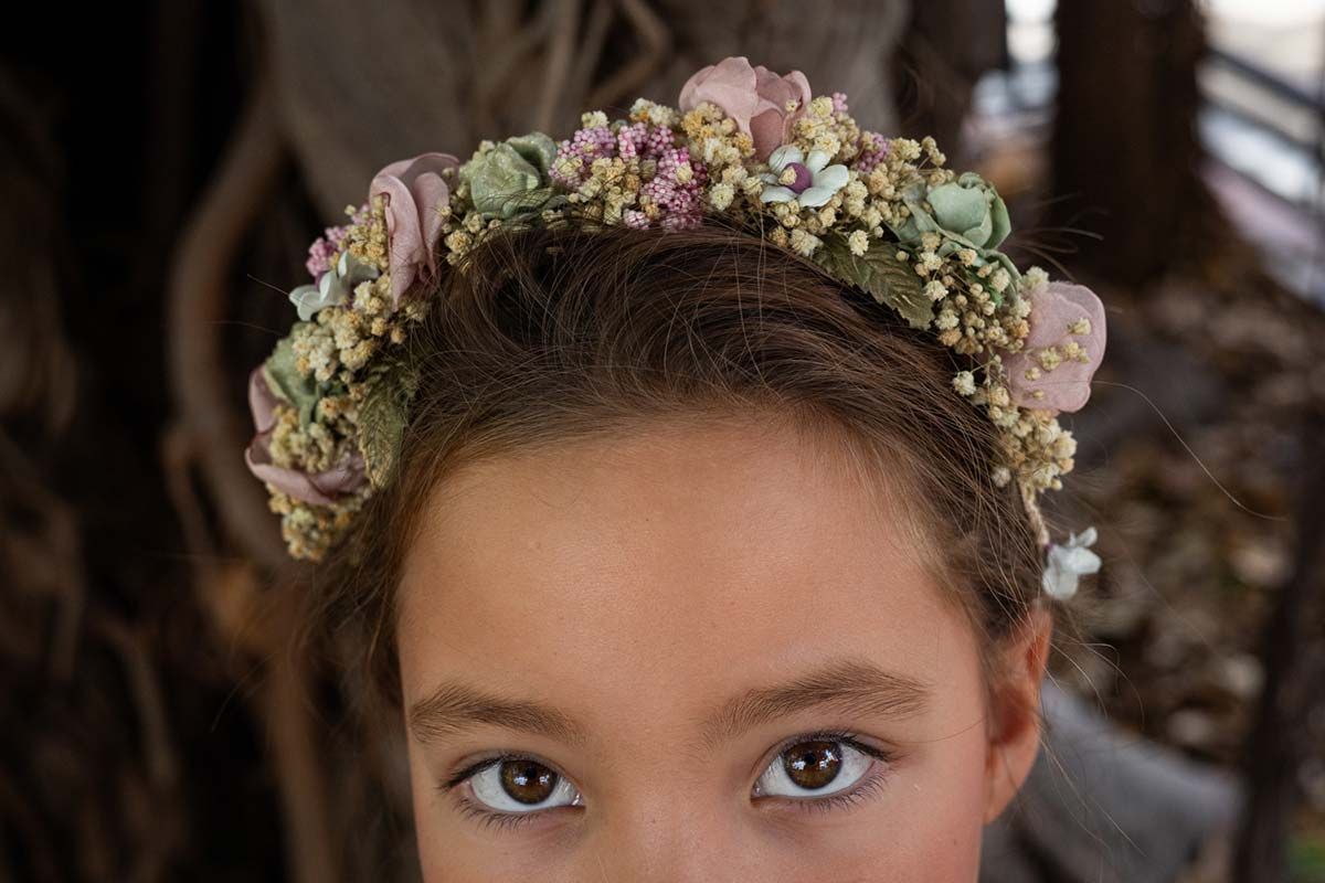 Retrato de un niño con una corona de flores, con expresión neutra sobre un fondo oscuro.