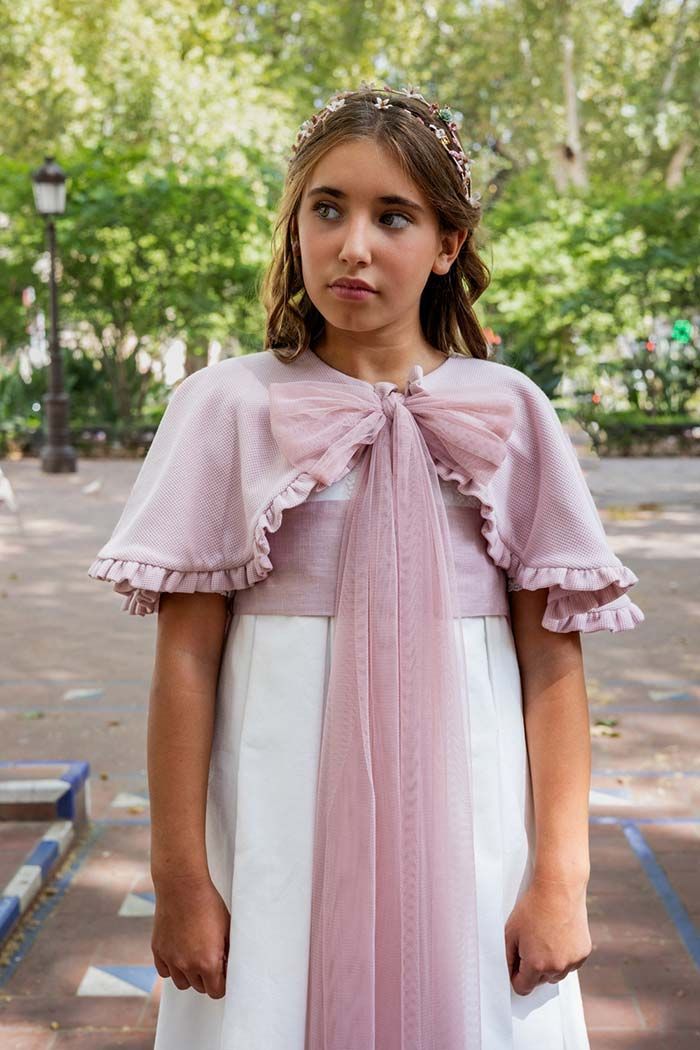 Niña con un vestido rosa y blanco de pie en un sendero arbolado al aire libre.