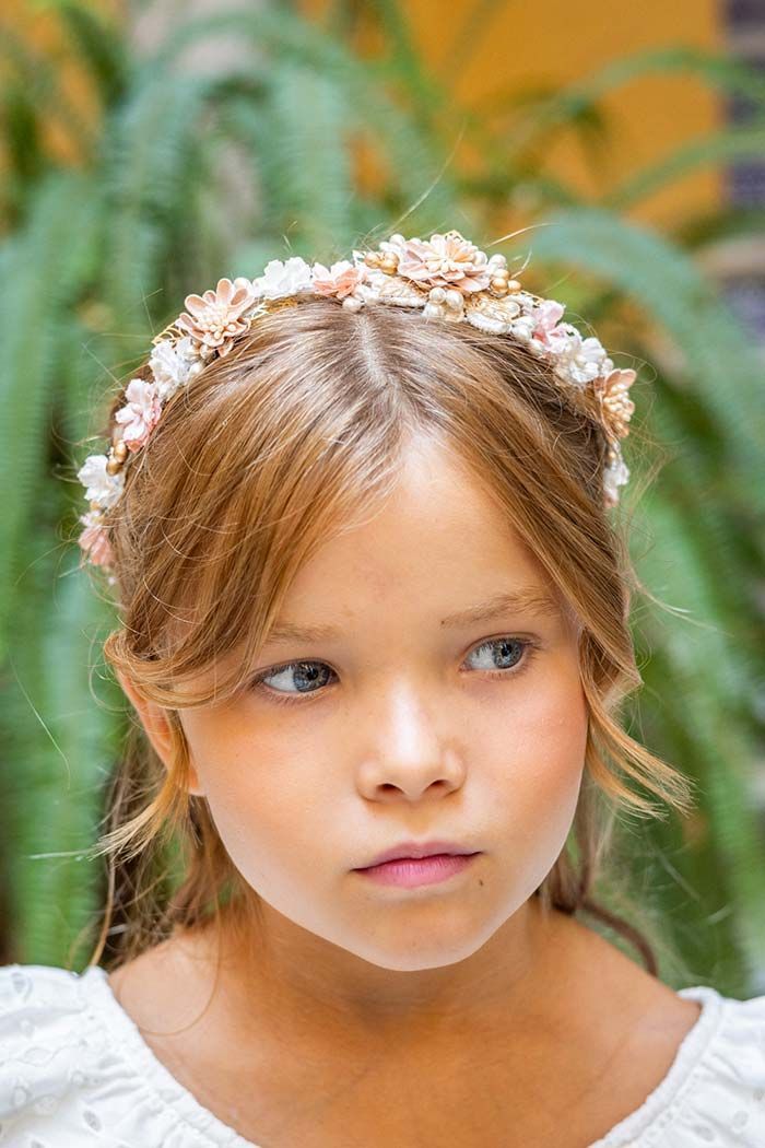 Niña con diadema floral, mirando hacia un lado con un fondo de hojas.