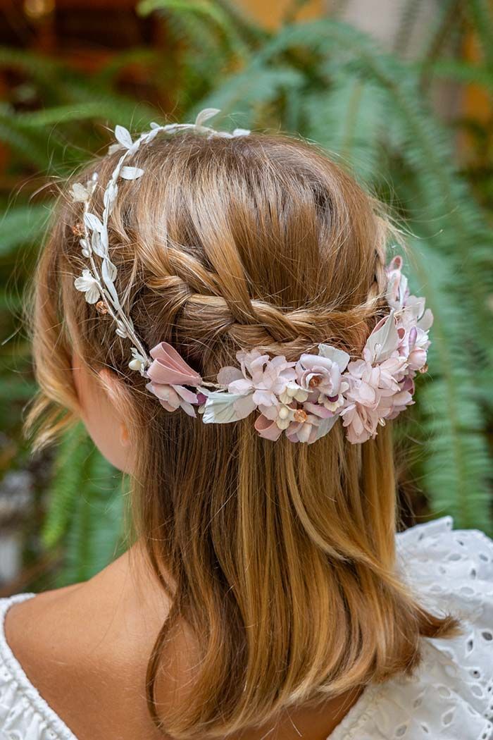 Vista trasera de una mujer rubia con una corona de flores en el cabello, al aire libre entre vegetación.