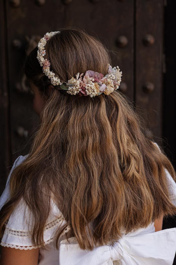 Vista trasera de una mujer con cabello largo y ondulado que lleva una corona de flores y un vestido blanco al aire libre.