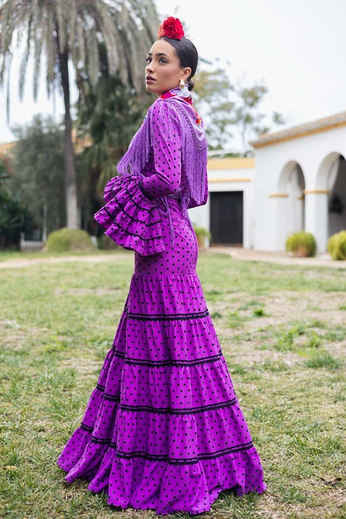 Mujer con un vestido morado brillante con volantes posando al aire libre sobre un césped cerca de arcos blancos.
