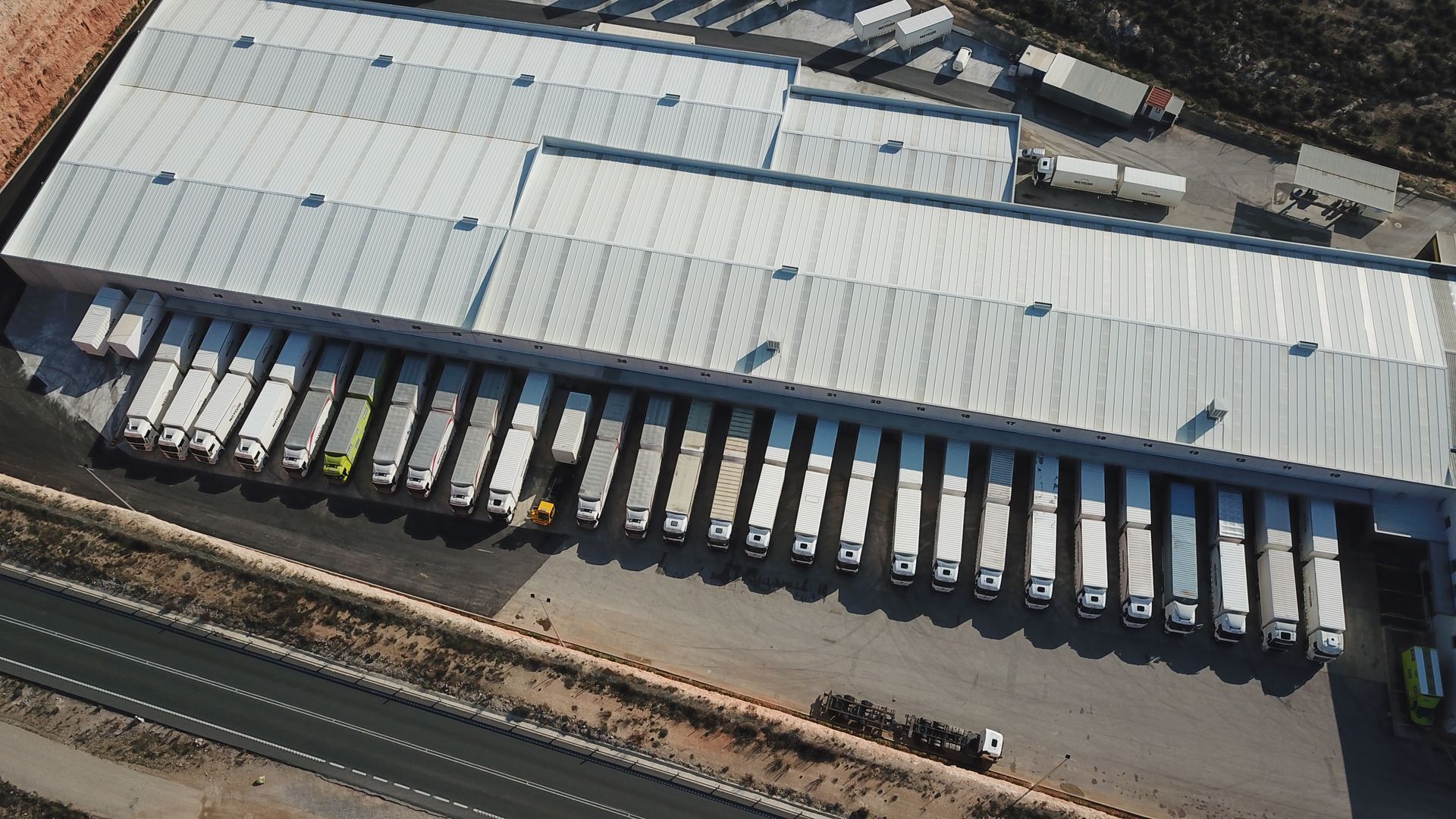 Almacén con numerosos semirremolques estacionados, bajo un gran techo metálico.