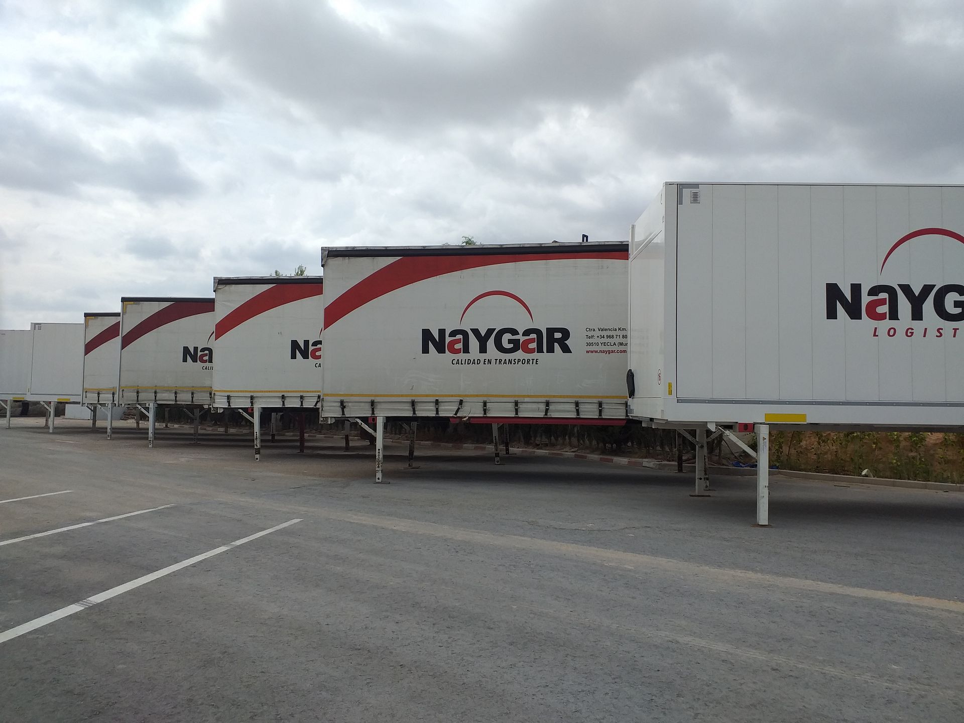 Remolques Naygar de color blanco estacionados en un estacionamiento de asfalto gris bajo un cielo nublado.
