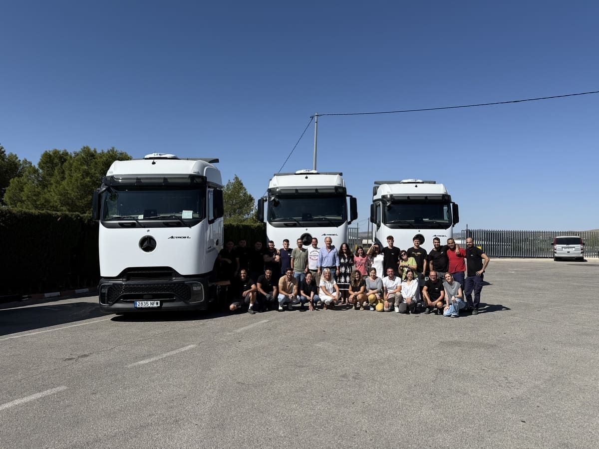 Grupo de personas de pie frente a tres camiones blancos en un día soleado.