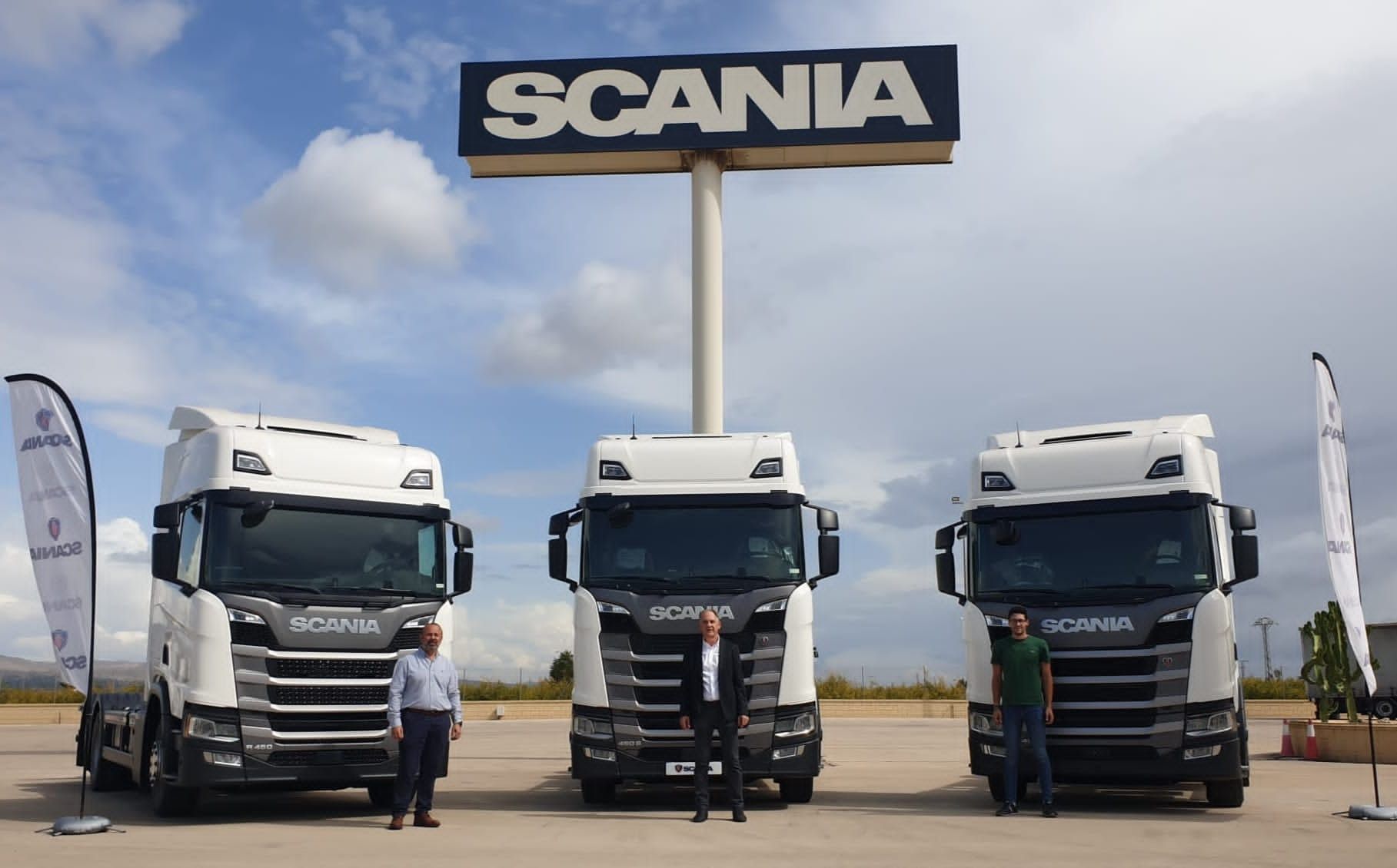 Tres camiones Scania blancos estacionados bajo un cartel de