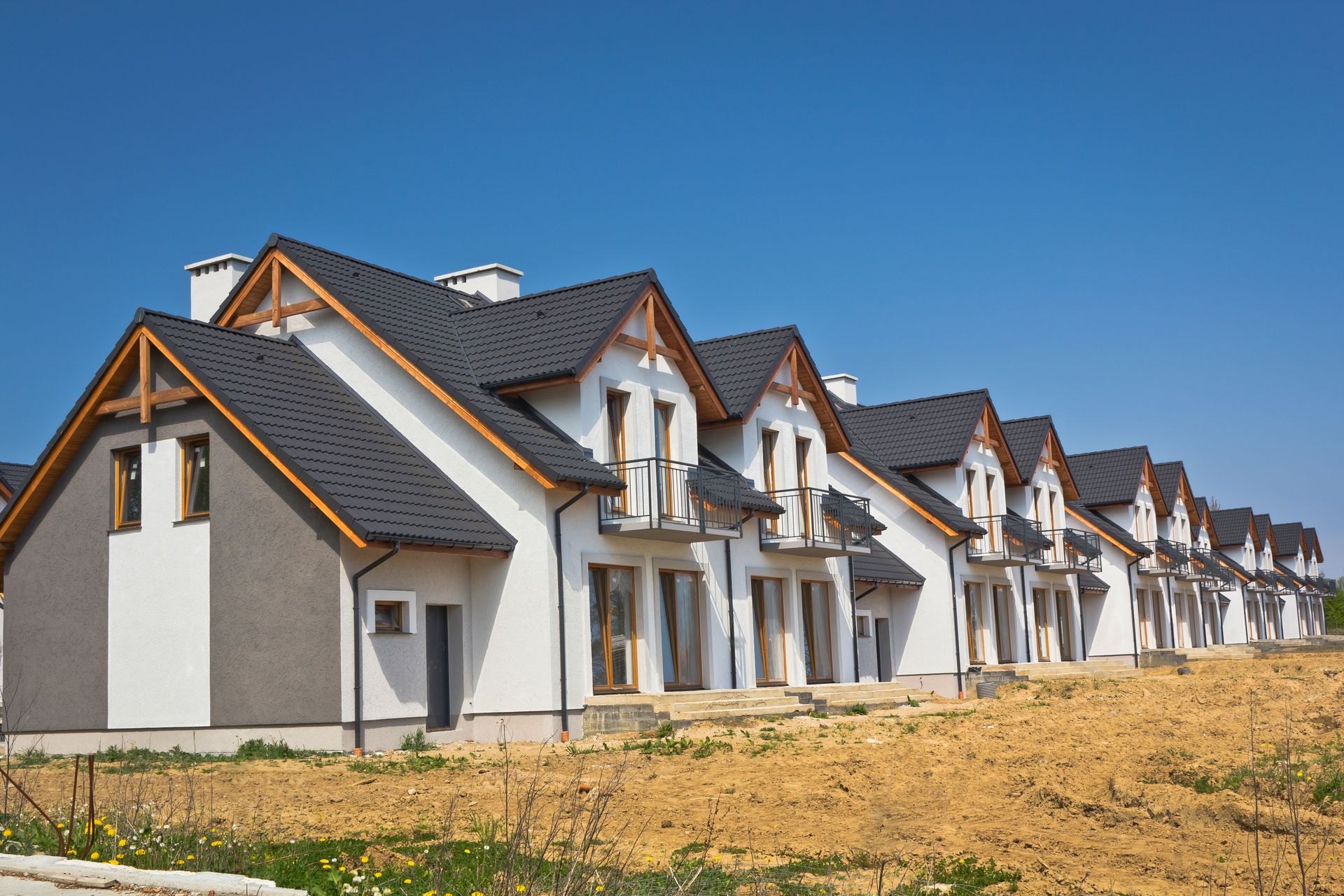 Una hilera de casas blancas con techos negros se encuentran sobre un campo de tierra.