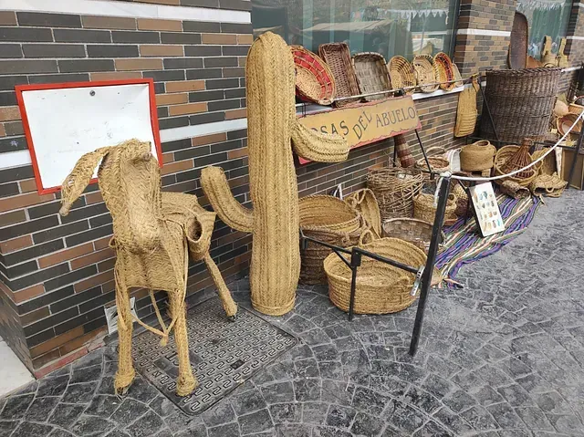Una estatua de un perro hecha de paja está sentada en la acera frente a un edificio de ladrillo.