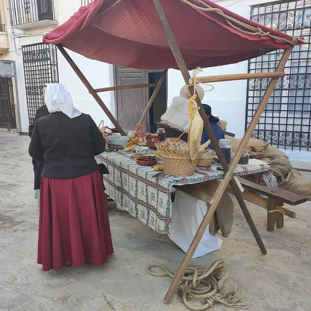 Una mujer con una falda roja está parada frente a una mesa bajo un dosel rojo.