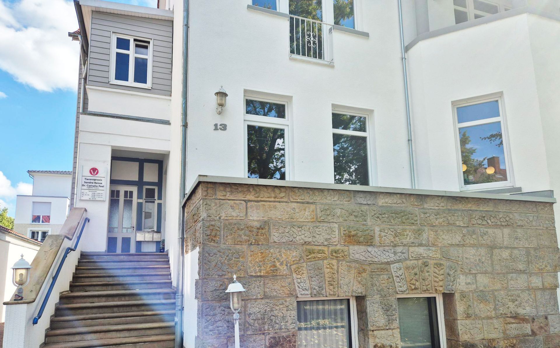 Weißes Gebäude mit Steinmauer, Stufen führen zu einer blauen Tür, Nummer 10 über den Fenstern.