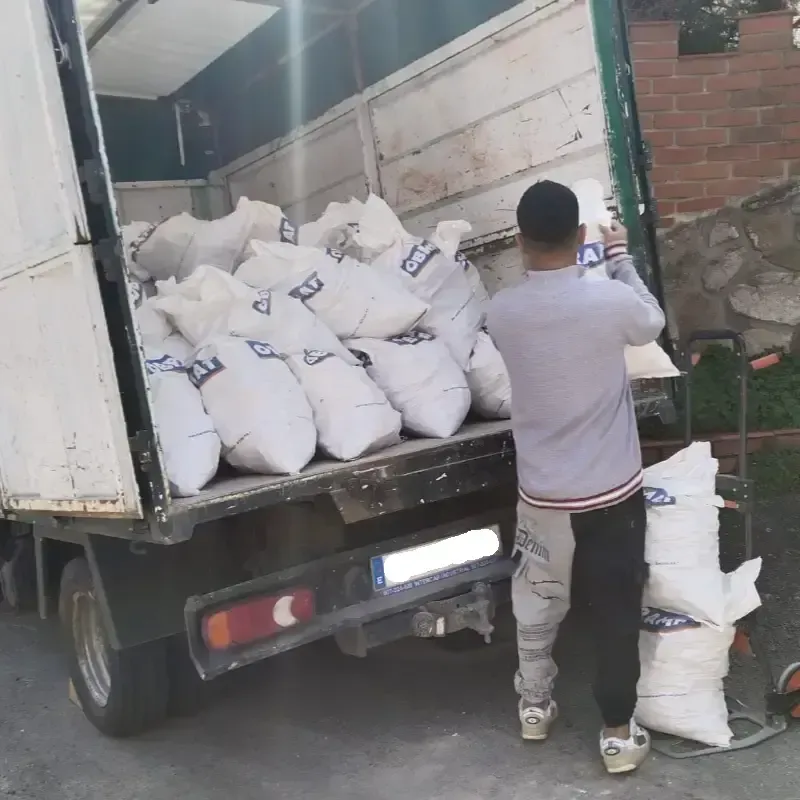 Un hombre carga bolsas blancas en la caja de una camioneta. La camioneta está abierta. El escenario es al aire libre.