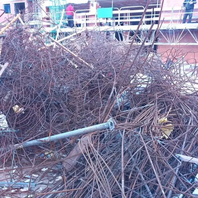 Pila de barras de refuerzo y tubos de metal enredados y oxidados en un sitio de construcción.
