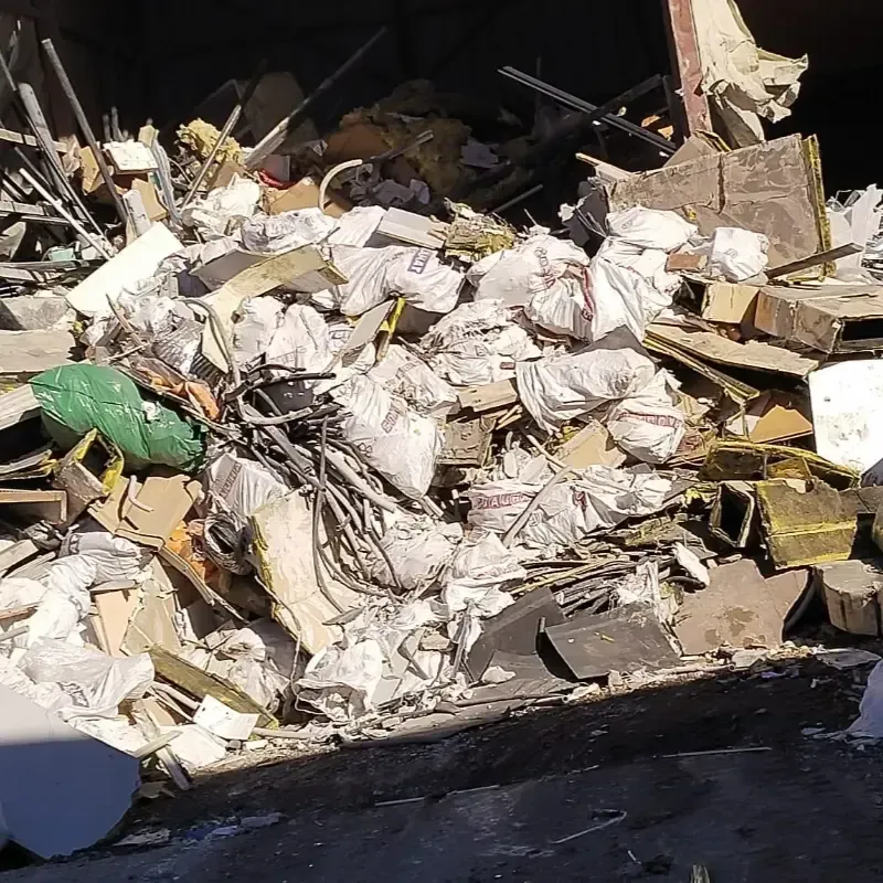 Montón de escombros de construcción, incluidas bolsas blancas, madera y metal, al aire libre bajo la luz del sol.