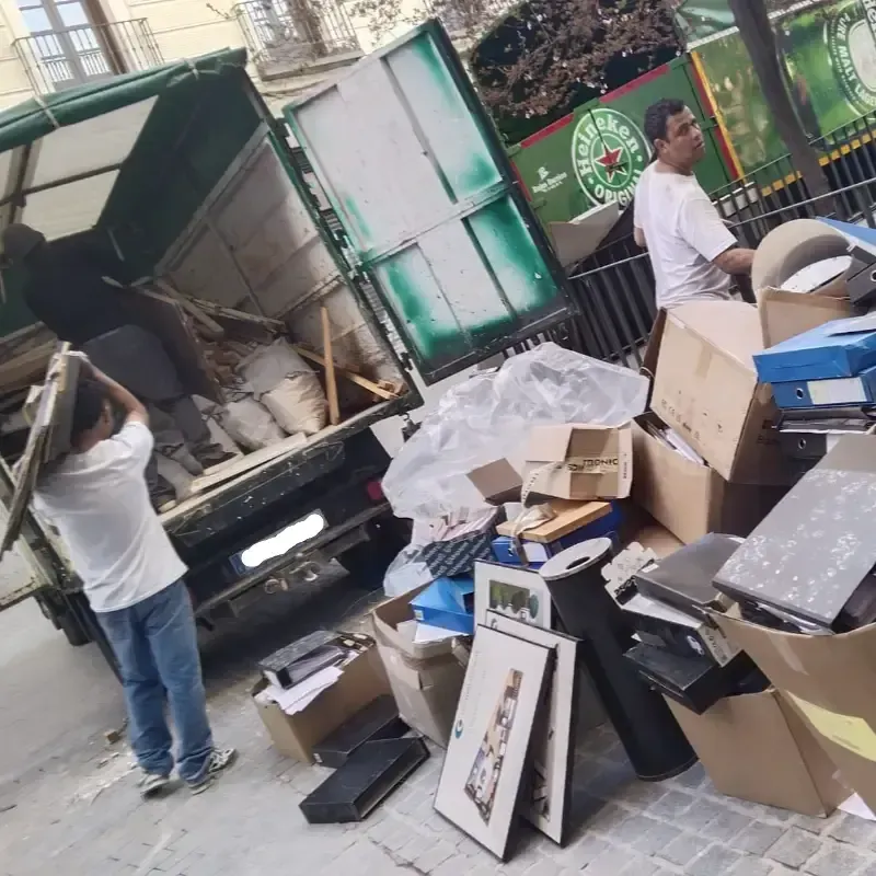 Hombres cargan artículos desechados, incluidas cajas, en un camión verde estacionado en una calle de la ciudad.