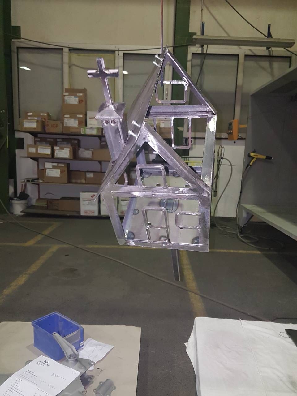 Eine Metallkonstruktion, die einer Kirche ähnelt, hängt in einer Werkstattumgebung an einem Haken.