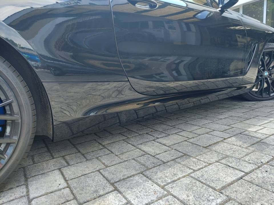 Ein schwarzer Sportwagen parkt auf Ziegelpflaster, seine Seitenwand spiegelt sich darin.