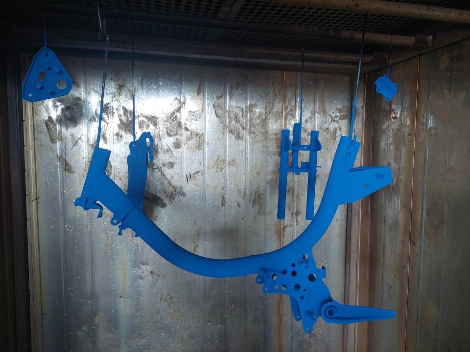 Blau lackierte Metallteile hängen zum Aushärten in einem Industrieofen.