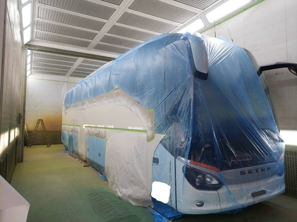 Der Bus steht in der Lackierkabine, ist teilweise mit blauer Plastikfolie und Klebeband abgedeckt und bereit zum Lackieren.