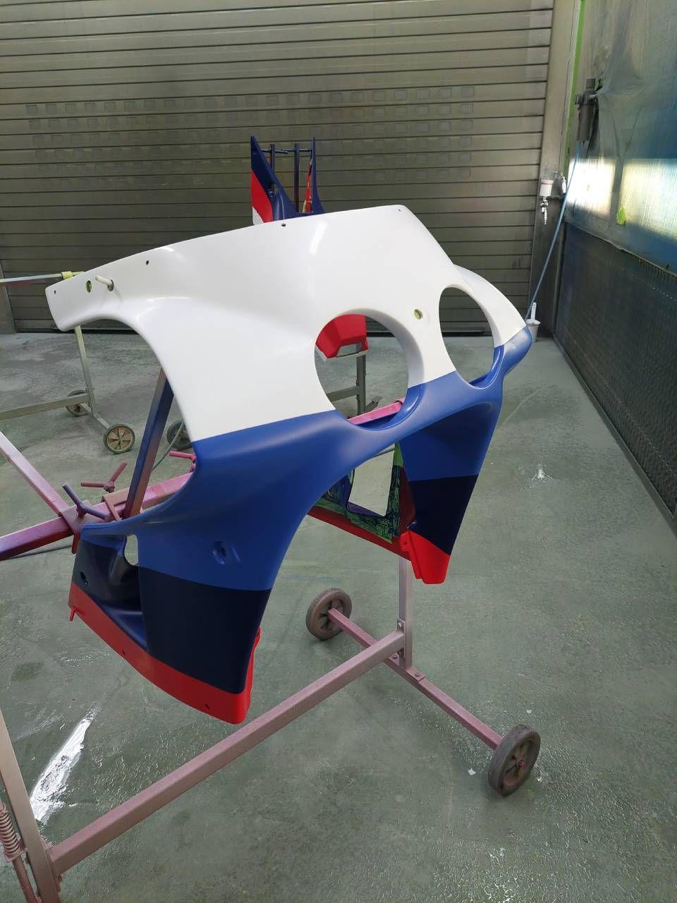 Motorradverkleidung, weiss, blau und rot lackiert, auf einem Ständer in einer Lackierkabine.