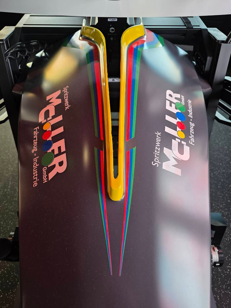 Schwarzes Fahrzeug mit gelb-rot-grün-blauem Design. „Müller“-Logo auf jeder Seite.
