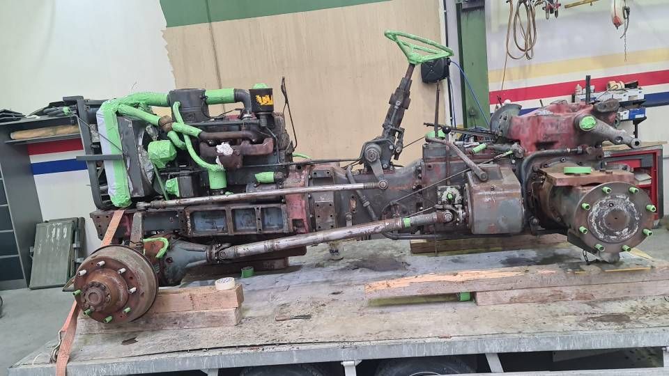 Ein unvollständiges, dunkel gefärbtes Traktorchassis mit Motor auf einem Pritschenwagen, mit grünen Akzenten.