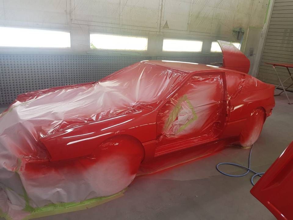 Ein rotes Auto, mit Plastikfolie abgedeckt, befindet sich während des Lackiervorgangs in einer Lackierkabine.