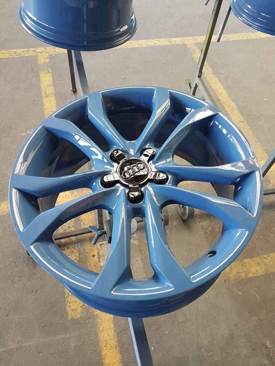 Blaues Autorad mit schwarzer Nabenkappe, auf einem Ständer in einer Werkstatt.