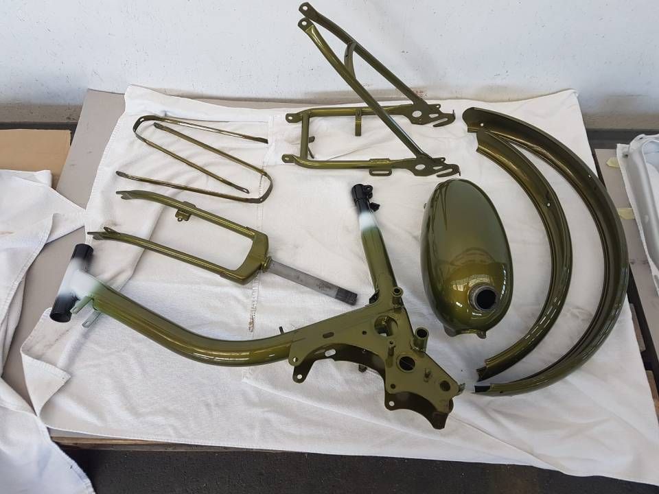 Teile eines zerlegten olivgrünen Rollers liegen auf einer weissen Fläche.