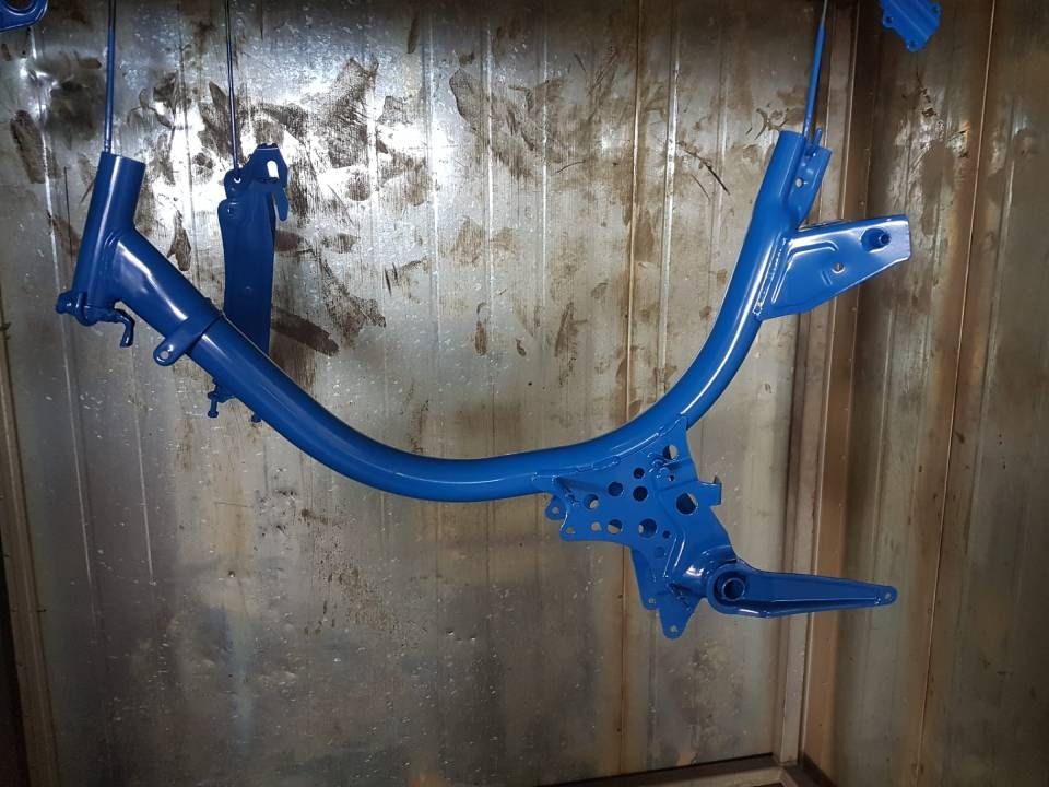 Blau lackierter Motorradrahmen hängt in einer Lackierkabine.